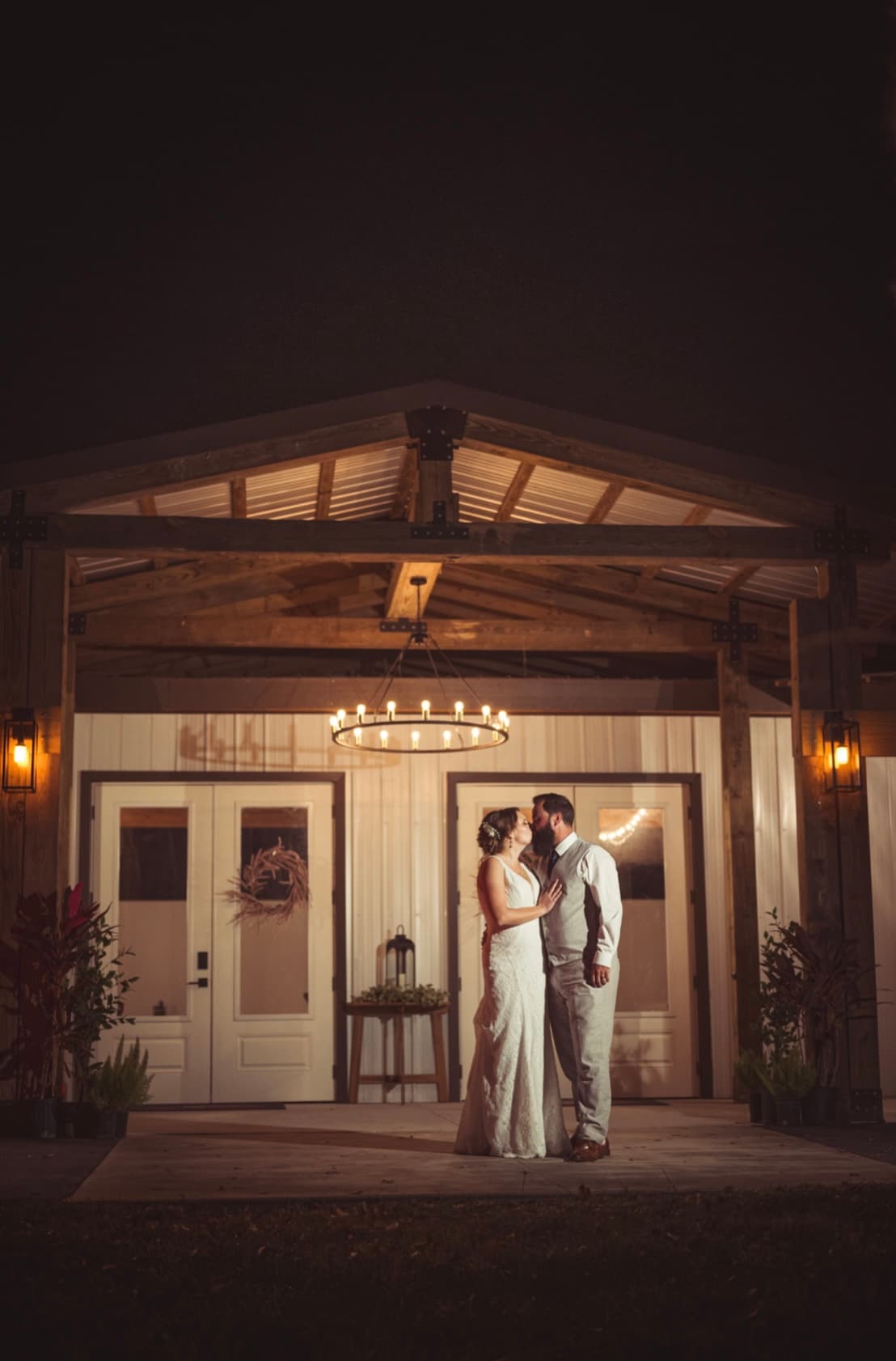 A couple kissing at the barn entrance under a candlelit chandelier, The Venue at Hidden Acres