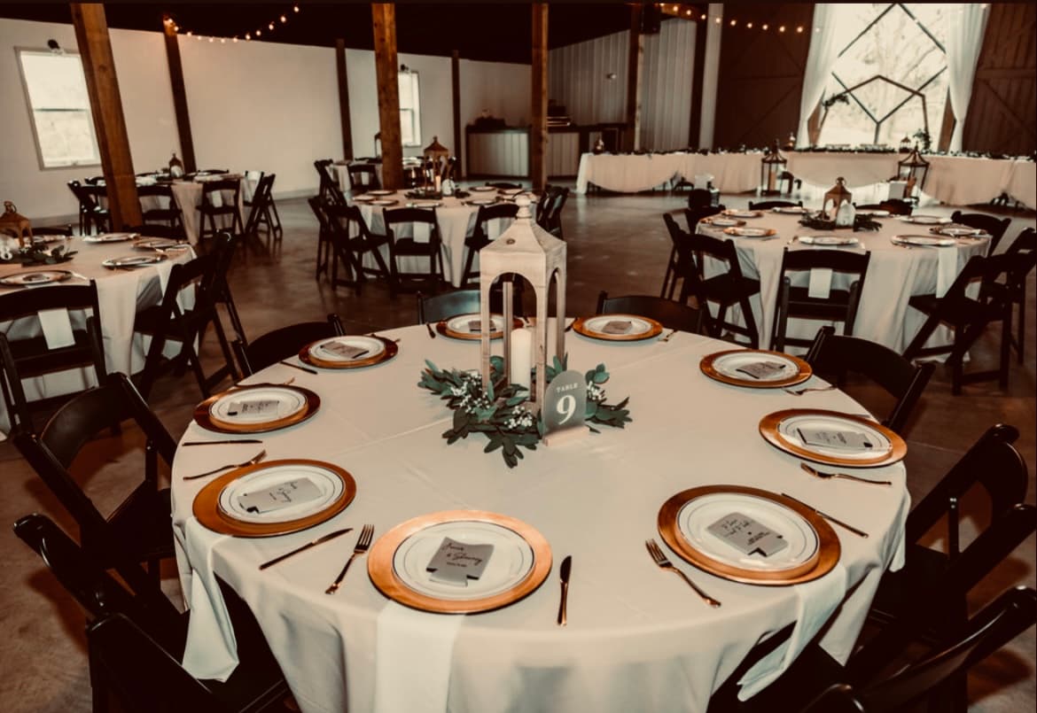 A reception table set with gold-rimmed chargers and greenery
